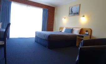 a hotel room with a blue carpeted floor , a double bed , and a television mounted on the wall at Torquay Tropicana Motel