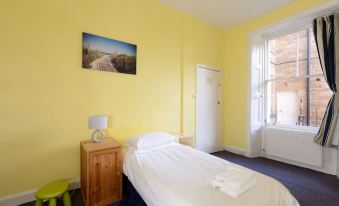 a room with a white bed , yellow walls , and a window in the background at Driftwood