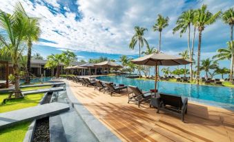 a large wooden deck surrounding a swimming pool , with several lounge chairs and umbrellas placed around it at La Vela Khao Lak