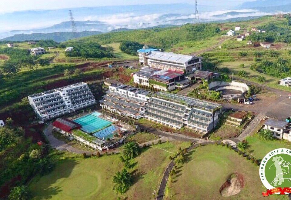 aerial view of a large resort complex surrounded by green hills and trees , with a golf course in the foreground at Cikidang Plantation Resort