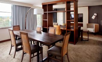 a wooden dining table surrounded by chairs in a room with a large window and a tv at Raleigh Marriott Crabtree Valley