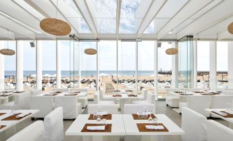 a modern restaurant with white tables and chairs , large windows , and a view of the beach at Tivoli Marina Vilamoura