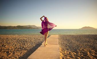 a woman in a purple dress is dancing on a wooden boardwalk near the ocean at Jiva Beach Resort - Ultra All Inclusive