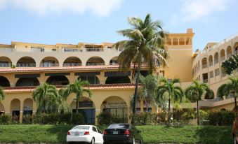 a parking lot with two cars parked in front of a large building , surrounded by palm trees at Park Royal Homestay Club Cala Puerto Rico