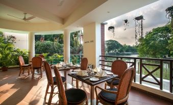 a dining room with a table set for a meal , surrounded by chairs and a balcony overlooking a lake at Hotel Grand Park Barishal