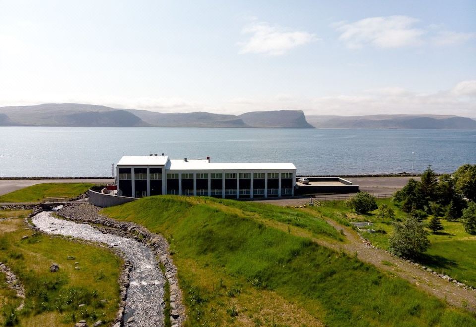 a modern building is situated on a hillside near a body of water , with mountains in the background at Fosshotel Westfjords