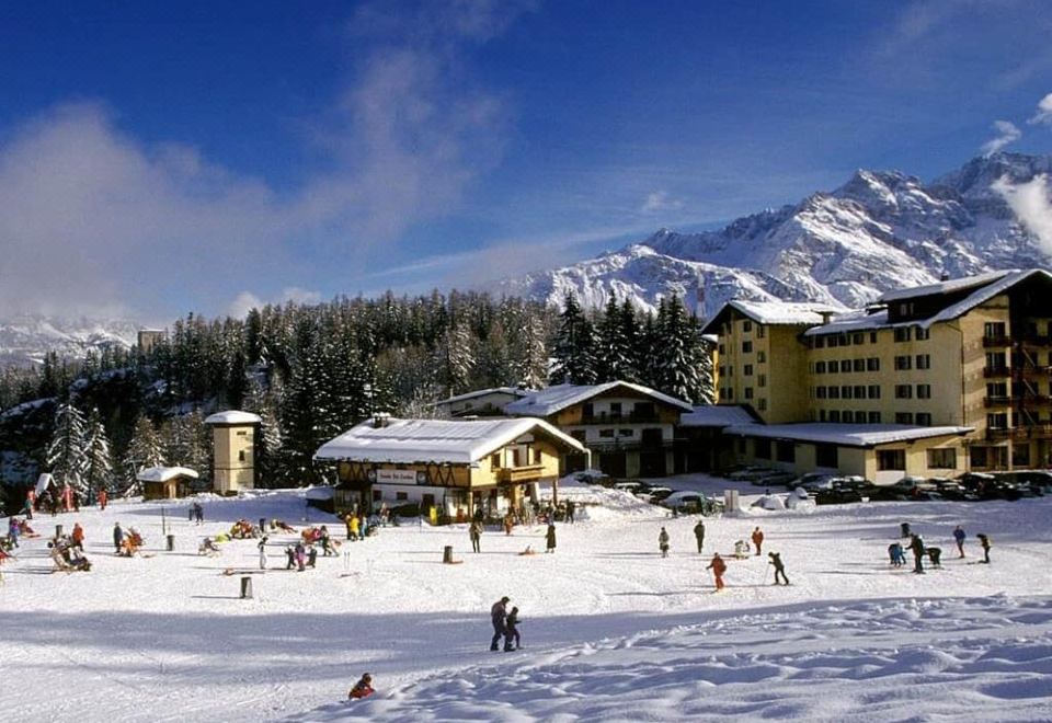 a group of people skiing and snowboarding on a snowy slope , with mountains in the background at Hotel Villa Argentina