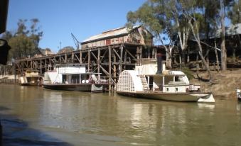 a boat is docked at a pier next to another boat in a river , with a wooden structure on the other side at Echuca Motel
