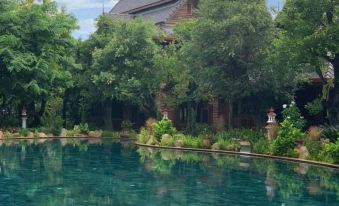 a large pool surrounded by lush green trees , with a building in the background and a blue sky overhead at Khum Wang Nuea Villa