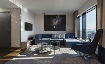 a modern living room with a blue couch , coffee table , and large windows overlooking the city at Scandic Havet