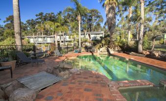 a small backyard with a pool surrounded by palm trees and a brick patio , creating a relaxing atmosphere at Fairway Motor Inn