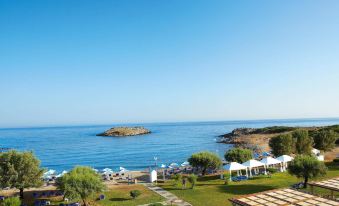 a beautiful beach scene with a group of people enjoying their time on the sandy shore at Grecotel Meli Palace
