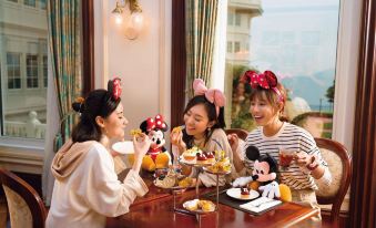 A couple is sitting at a table with food and drinks in front of them, while another woman is holding something at Hong Kong Disneyland Hotel