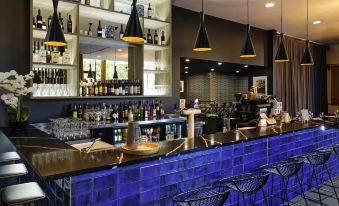 a modern bar with a long counter , blue tiles , and various bottles and glasses on display at Mantra Albury Hotel
