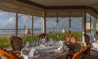 a dining room with a table set for a meal , surrounded by chairs and overlooking a body of water at Sandhouse Hotel