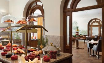 a well - lit room with a dining table , two trays of food , and an open door leading to a patio at Falkenstein Grand, Autograph Collection