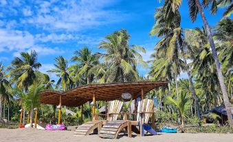 a tropical beach scene with palm trees , a wooden gazebo , and a row of lounge chairs under the shade at Coconut Garden Beach Resort