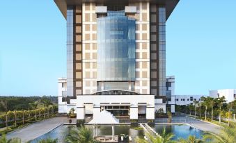 a large building with a tall glass and metal structure is surrounded by palm trees at Le Meridien Coimbatore