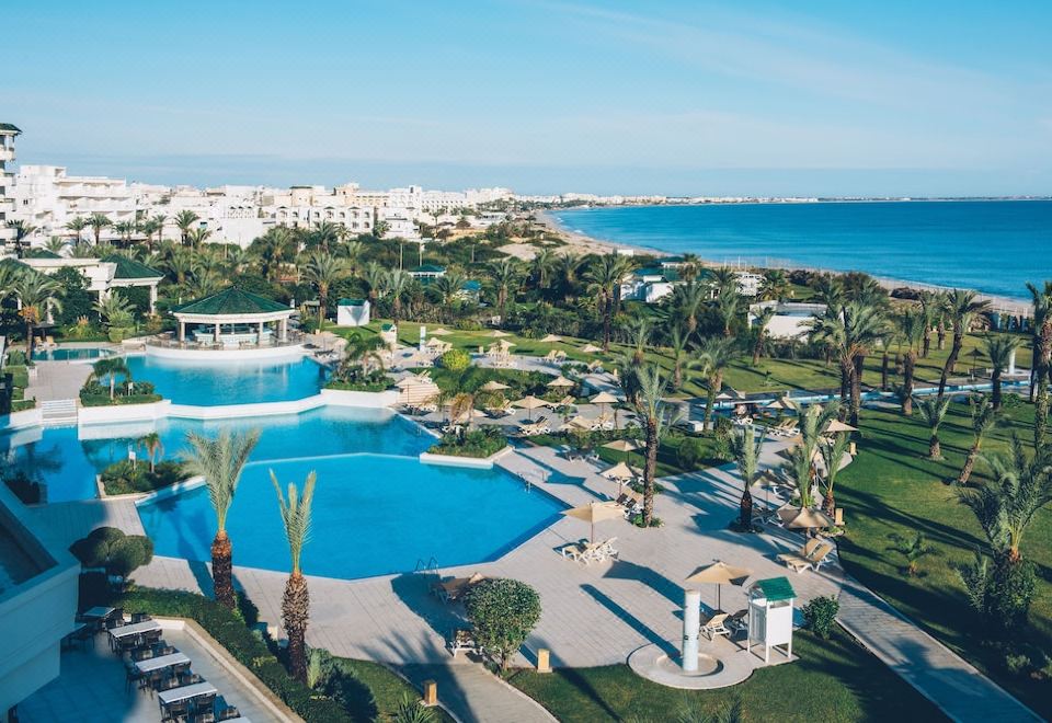 a large outdoor swimming pool surrounded by palm trees and lush greenery , with a city skyline visible in the background at Iberostar Selection Royal El Mansour