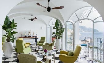 a modern living room with a view of the ocean , featuring green chairs and white tables at Hotel Miramalfi