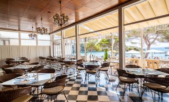 an empty restaurant with a checkered floor and large windows overlooking a pool area , surrounded by wicker chairs and tables at THB Felip - Adults Only