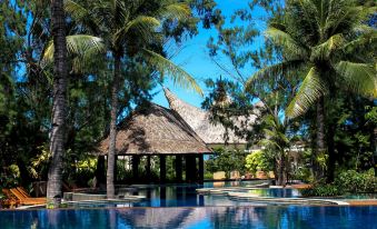 a large swimming pool with a thatched roof structure in the background , surrounded by palm trees and lush greenery at Aston Sunset Beach Resort - Gili Trawangan
