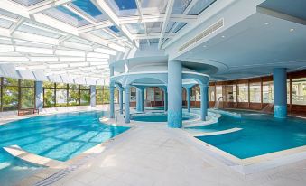 an indoor swimming pool with a white ceiling and walls , surrounded by glass windows and blue columns at Mitsis Galini