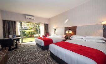 a hotel room with two beds , each bed has a red blanket and is positioned near a sliding glass door at Waipuna Hotel & Conference Centre