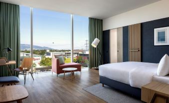 a modern hotel room with a large window offering a view of the city , a bed , and a chair at Four Points by Sheraton Panoramahaus Dornbirn
