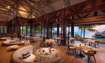 a restaurant with wooden tables and chairs , a bar area , and a view of the ocean at Conrad Bora Bora Nui