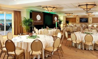 a large dining room with multiple round tables , chairs , and a stage set up for an event at Riverside Hotel