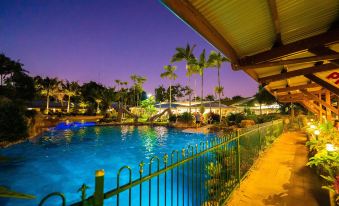 a large pool with a fence around it and palm trees in the background at night at Cairns Colonial Club Resort