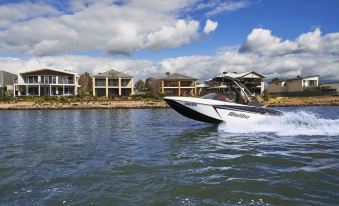 a white and black speedboat is speeding across the water near a row of houses on a sunny day at The Sebel Yarrawonga Silverwoods
