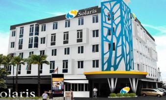 a large , modern building with a blue and white facade , surrounded by palm trees and other buildings at Solaris Hotel Malang