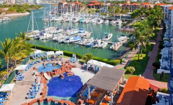 a beautiful marina with multiple boats docked in the water , surrounded by lush greenery and buildings at El Cid Marina Beach Hotel