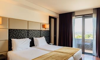 a modern hotel room with two beds , white bedding , and gold accents , near a window with a view of the city at Axis Porto Business & Spa Hotel