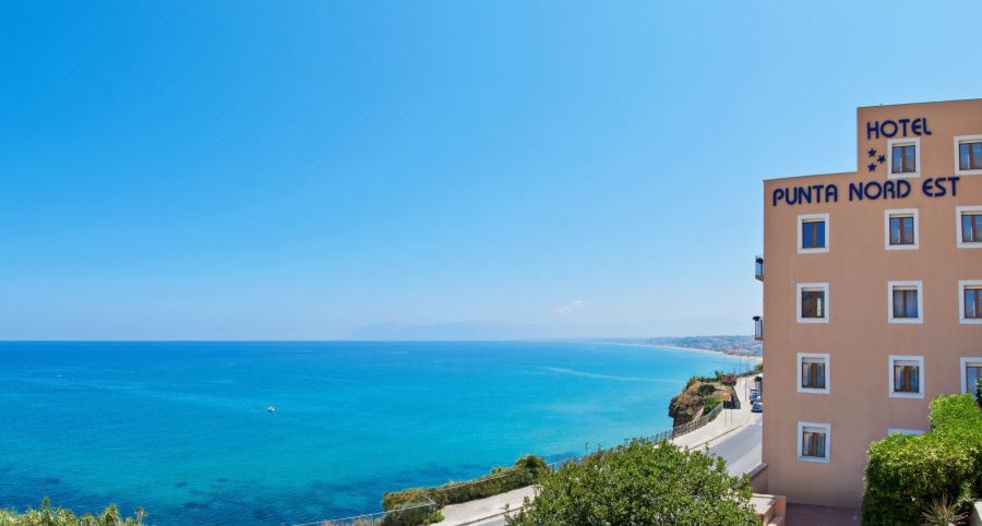 a scenic view of the ocean with a road winding through the foreground and clear blue skies at Hotel Punta Nord Est