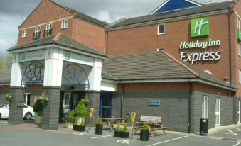 a holiday inn express hotel with its name displayed on the building , and several wooden chairs placed in front of it at Holiday Inn Express Newcastle Gateshead