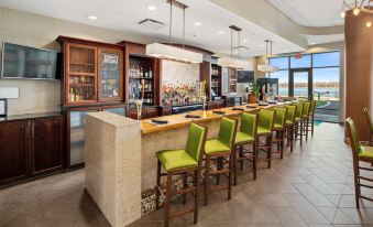 a modern restaurant with a long bar counter , several chairs , and a window overlooking the ocean at Holiday Inn Owensboro Riverfront