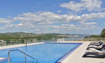 a large , empty swimming pool with a clear blue water and surrounding outdoor facilities , set against a backdrop of mountains and clouds at Hotel Panorama