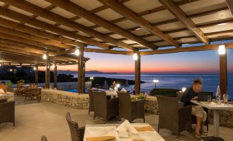 a restaurant with a beautiful view of the ocean at sunset , surrounded by chairs and tables at Lena Beach Hotel