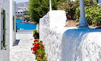 a white building with red flowers on the balcony , overlooking a blue sea and white buildings at Mykonos Beach Hotel