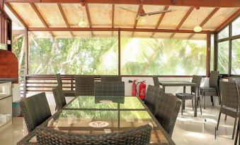 a glass dining table with chairs is set up under a covered patio area , surrounded by trees at Liberty Guesthouse Maldives