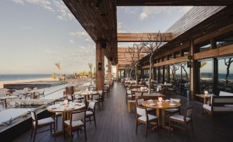 an outdoor dining area with wooden tables and chairs , surrounded by trees and overlooking a body of water at Nobu Hotel Los Cabos