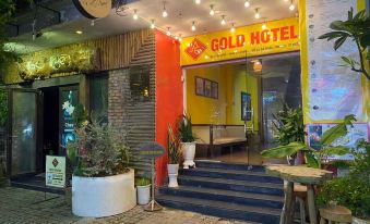 a small hotel with a neon sign above the entrance , surrounded by potted plants and trees at Gold Hotel