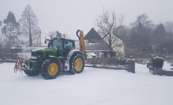 a green tractor is driving on a snow - covered road , with a house in the background at The Nobody Inn