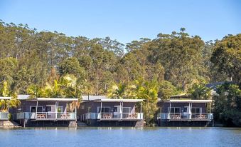 a row of floating homes on the edge of a body of water , surrounded by trees at Ingenia Holidays Lake Conjola