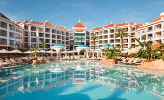 a large hotel with a pool surrounded by lounge chairs and umbrellas , providing a relaxing atmosphere at Hilton Vilamoura As Cascatas Golf Resort & Spa