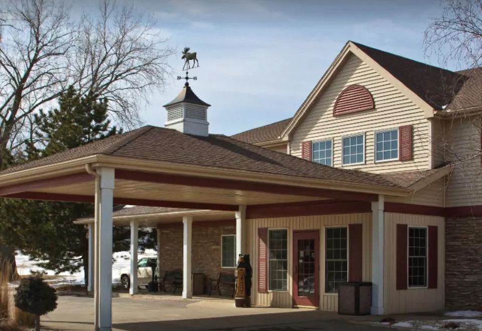 a large building with a covered porch and a clock tower on top , located in a rural area at Boarders Inn & Suites by Cobblestone Hotels – Waukon