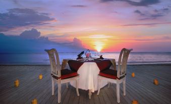 a table with a white tablecloth and red pillows is set up on a wooden deck overlooking the ocean at Aston Sunset Beach Resort - Gili Trawangan